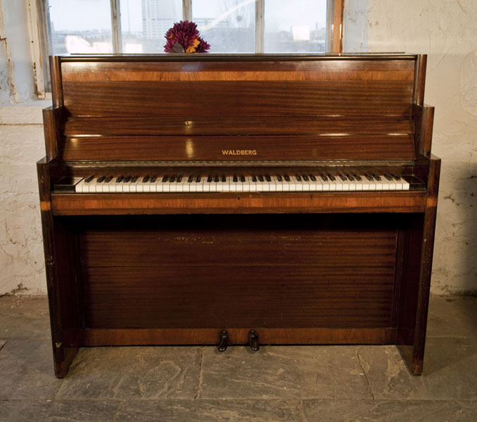 Art-Deco style, Waldberg upright piano with a polished, mahogany case. Cabinet features strong geometric styling with walnut crossbanding accents. Piano has eighty-five notes and two pedals