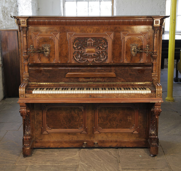 An 1898, Steingraeber upright piano with a walnut case, Cabinet features a carved, Neoclassical style filgree panel and ornate brass candlesticks. Piano has an eighty-eight note keyboard and two pedals.