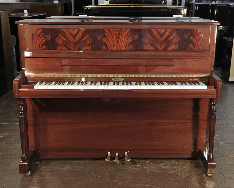 A Kemble upright piano with a mahogany case and flame mahogany panel. Piano has an eighty-eight note keyboard and and three pedals