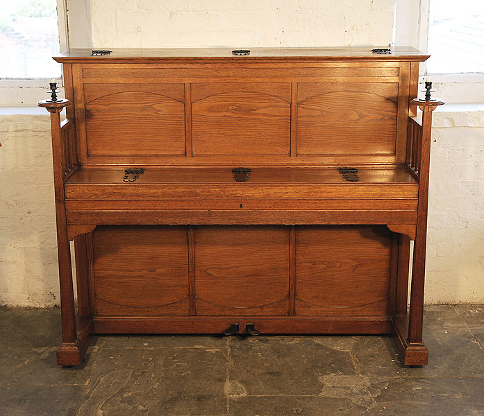 A 1903, Arts and Crafts style, Bluthner upright piano with a polished, oak case. Piano features  large, sculptural candlesticks and ornate, iron hinges. Piano has an eighty-eight note keyboard and two pedals.