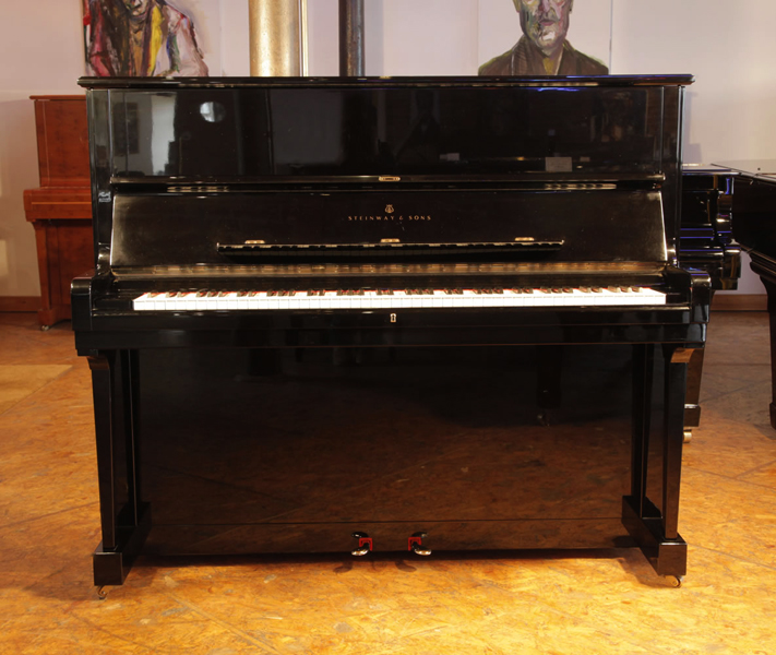 A 1985, Steinway Model V upright piano with a black case and brass fittings. Piano has an eighty-eight note keyboard and three pedals.