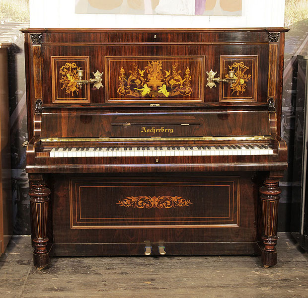A rebuilt, Ascherberg upright piano for sale with a rosewood case and baluster legs. Cabinet inlaid with Neoclassical design featuring flowers, urns, musical instruments, figures, shells and scrolling acanthus. Piano has an eighty-five keyboard and two pedals.