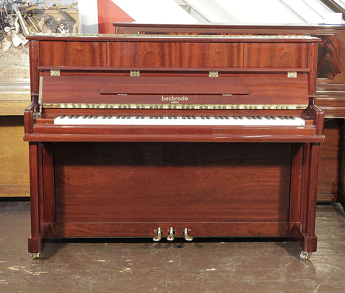 A brand new, Besbrode SU112 upright piano with a mahogany case and polyester finish. Piano hasan eighty-eight note keyboard and three pedals.