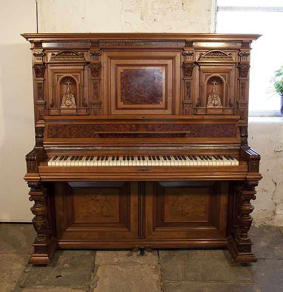 A German upright piano with a Neoclassical style walnut case and cup and cover legs. Cabinet features ornately carved pilasters in high reief and copper sconces in a sea monster design. Piano has an eighty-five note keyboard and two pedals