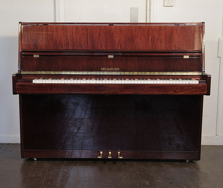 Neumayer upright piano with a mahogany case. Piano has an eighty-eight note keyboard and three pedals. 