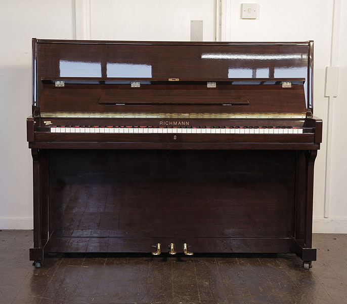 A Richmann upright piano with a mahogany case. Piano has an eighty-eight note keyboard and three pedals 