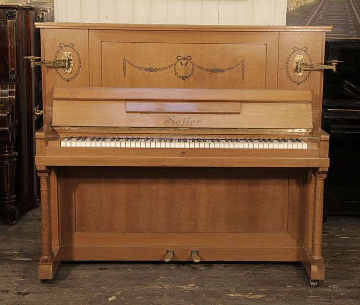 A reconditioned, 1911, Seiler upright piano for sale with a walnut case and two turned, column legs. Cabinet inlaid with contrasting ebony with stylised flowers, swags and bows. Piano has an eighty-five note keyboard and two pedals. 