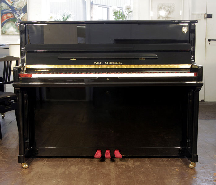 A brand new, Wilh Steinberg Model AT-K18 upright piano with a black case and brass fittings. Piano features a slow fall mechanism, eighty-eight note keyboard and three pedals. 