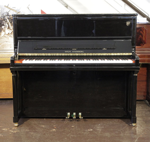 A Brand new, Wilh Steinberg Model AT-K30 upright piano with a black case and brass fittings. Piano features a walnut key block and slow fall mechanism. Piano has an eighty-eight note keyboard and three pedals. 
