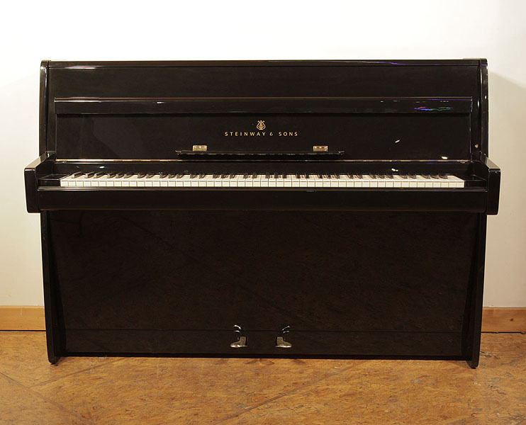 A 1961, Steinway Model F upright piano with a black case and brass fittings. Piano has an eighty-eight note keyboard and two pedals.