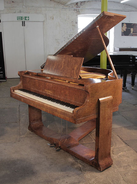 A 1936, Art Deco style, Chappell baby grand piano for sale with a quilted maple case. Cabinet features sculptural piano legs attached to a cross stretcher. Piano has an eighty-eight note keyboard and a two-pedal lyre.
