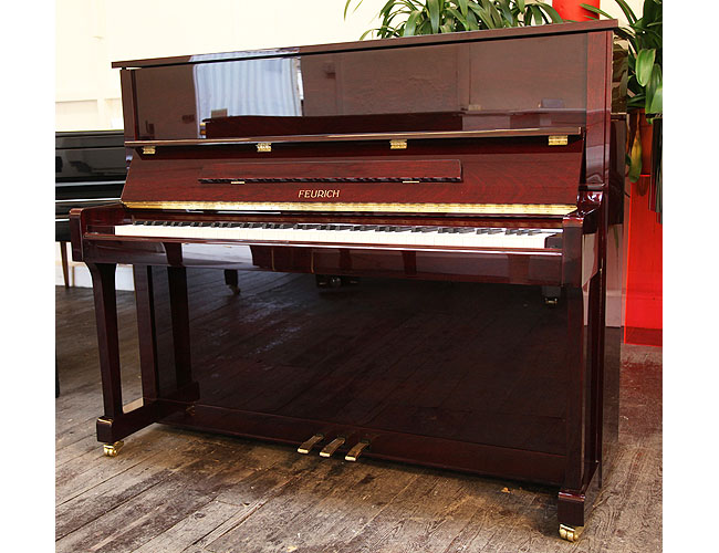 Brand new, Feurich Model 122 upright piano with a Bordeaux Gloss mahogany case and brass fittings.Piano has an eighty-eight note keyboard and three pedals. 