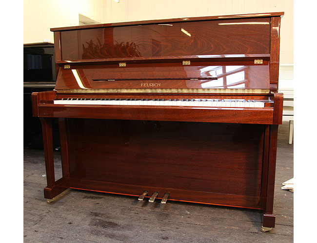 Brand new, Feurich Model 122 upright piano with a Walnut Gloss case and brass fittings. Piano has an eighty-eight note keyboard and three pedals. 