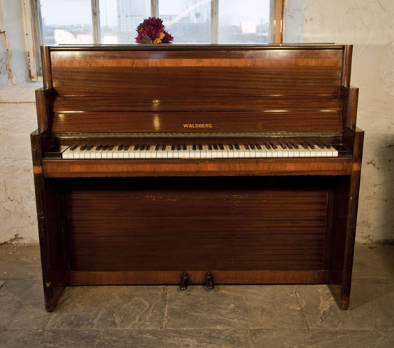 An Art-Deco Waldberg upright piano with a polished, mahogany case. Piano has an eighty-five note keyboard and two pedals
