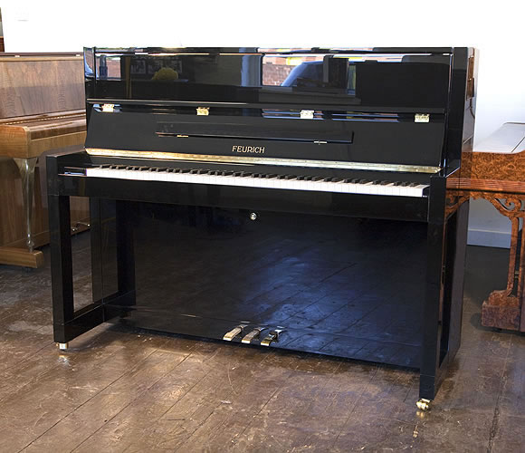 Brand New Feurich Model 115 upright piano with a black case and brass fittings. Piano has an eighty-eight note keyboard and  three pedals