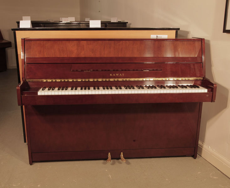 A 1985, Kawai CX-4S  upright piano for sale with a walnut case and brass fittings. Piano has an eighty-eight note keyboard and two pedals.  