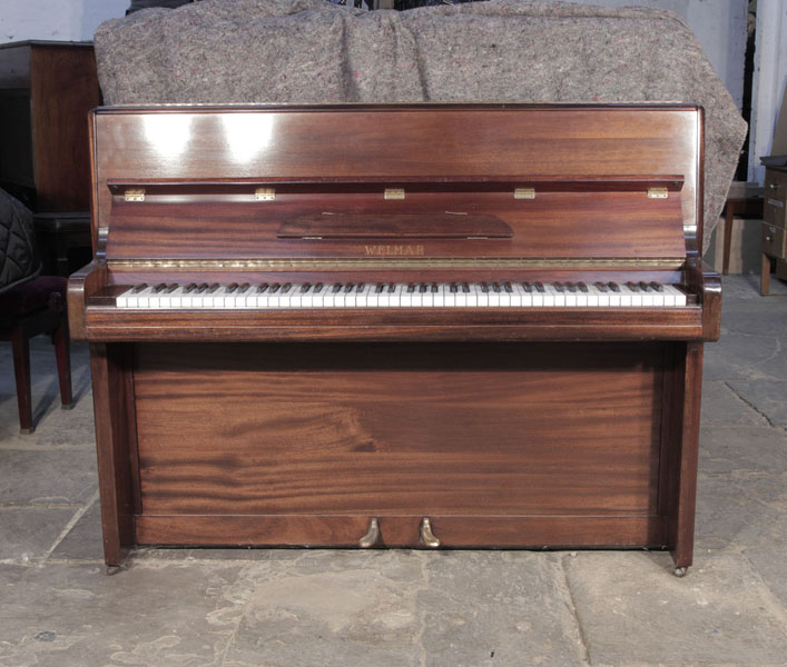 Pre-owned, 1953, Welmar upright piano with a mahogany case and brass fittings. Piano has an eighty-eight note keyboard and two pedals.