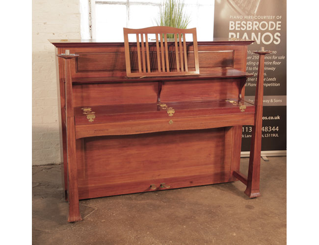 An 1899, Arts and Crafts style, Bechstein Model IV upright piano with a walnut case and sizeable, brass hinges. Pianos large architectural legs taper into candlesticks