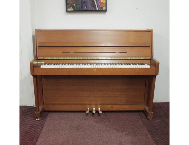 Pre-owned, Steinbach UP108M upright piano with a walnut case. Piano has an eighty-eight note keyboard and three pedals. 