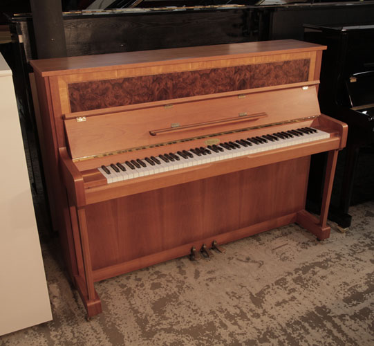 A 1992, Kemble upright piano with a crown-cut walnut case. Cabinet features a book-matched, burr walnut front panel. Piano has an eighty-eight note keyboard and three pedals. 